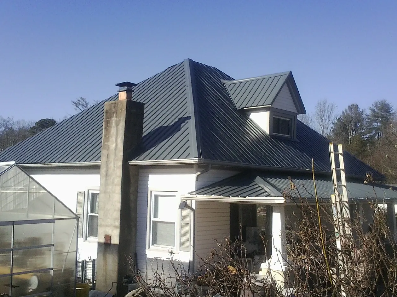 Dark blue standing seam metal roof on a white farmhouse with dormer — Slate & Tile Roof Repair by Roofing Brothers in East Liberty