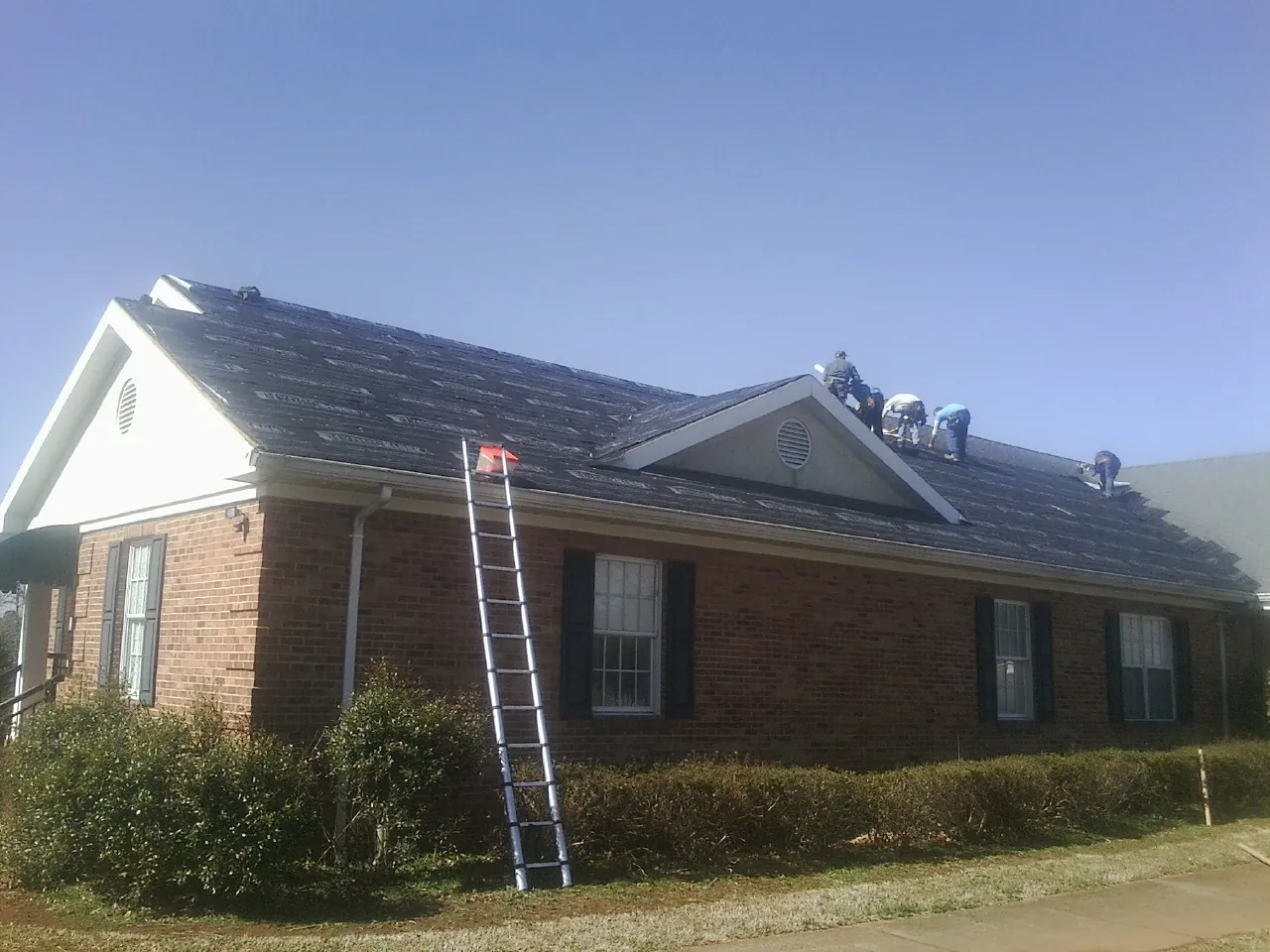 Crew tearing shingles off a brick ranch roof with a ladder set — Metal Roof Repair work by our crew in East Liberty