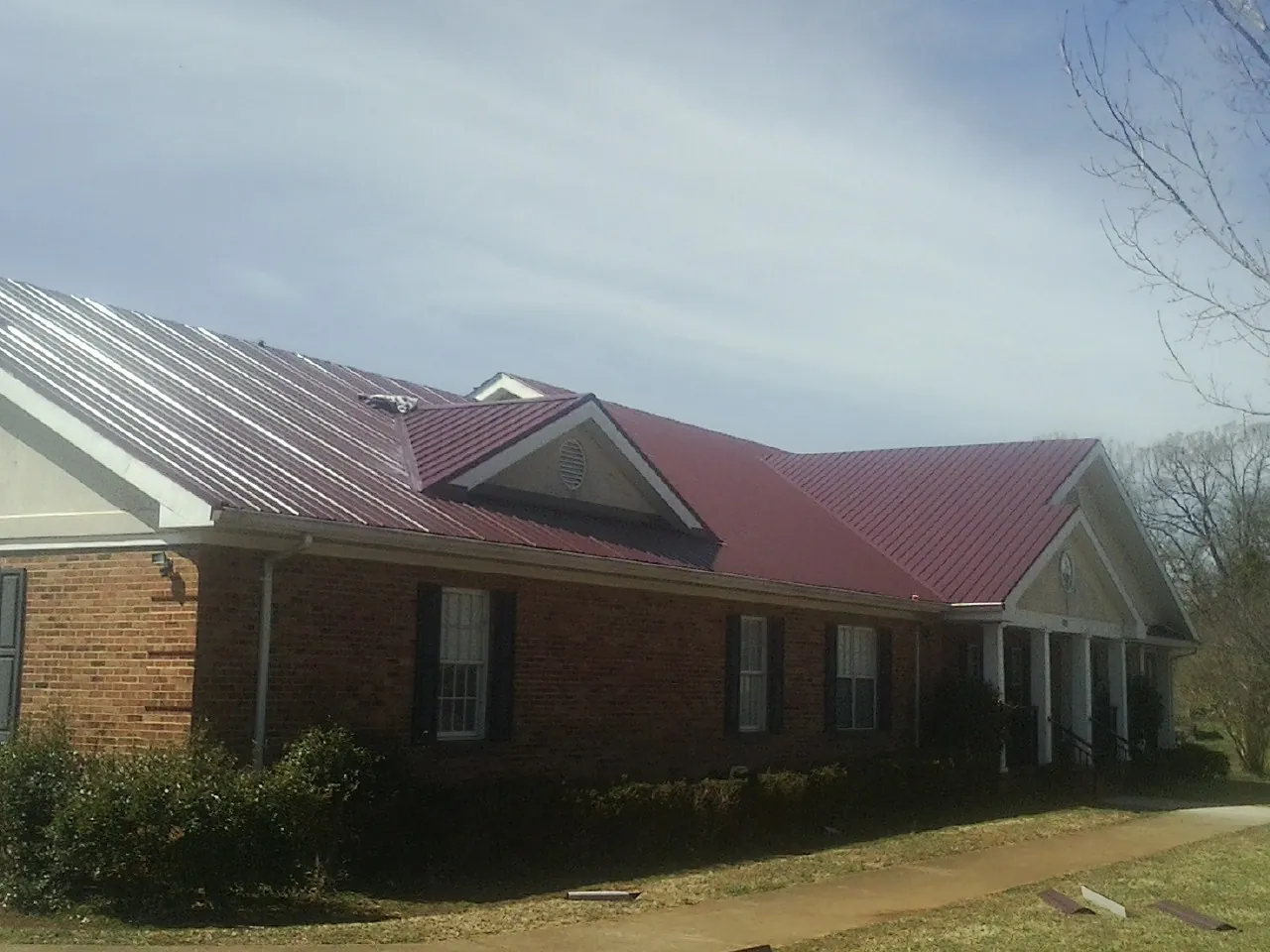 Red metal roof with gabled entries on a long brick building, from a Hail Damage Roof Repair job in East Liberty