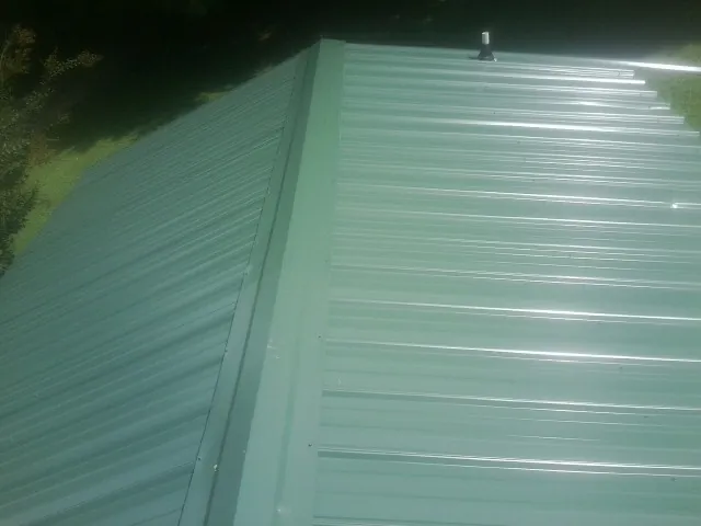 New green metal panels meeting at the ridge of a roof — Flat Roof Repair work by our crew in East Liberty