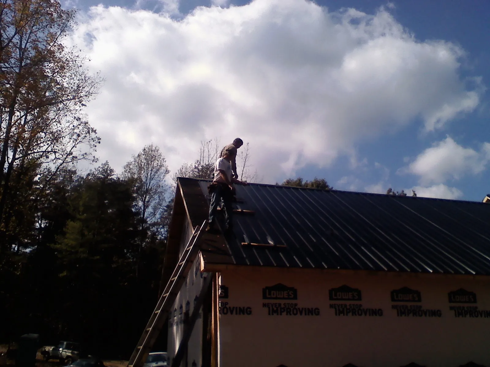 Roofer fastening dark metal panels high against a cloudy sky, from a Roof Inspection job in East Liberty