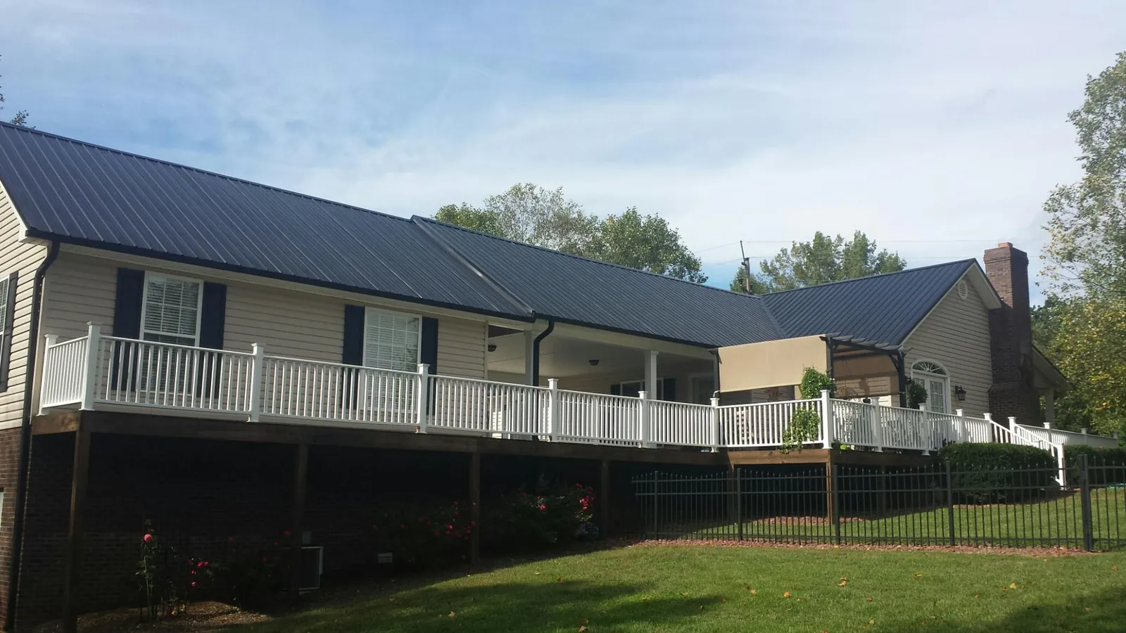 Black metal roof above a long white railed deck on a hillside home in East Liberty