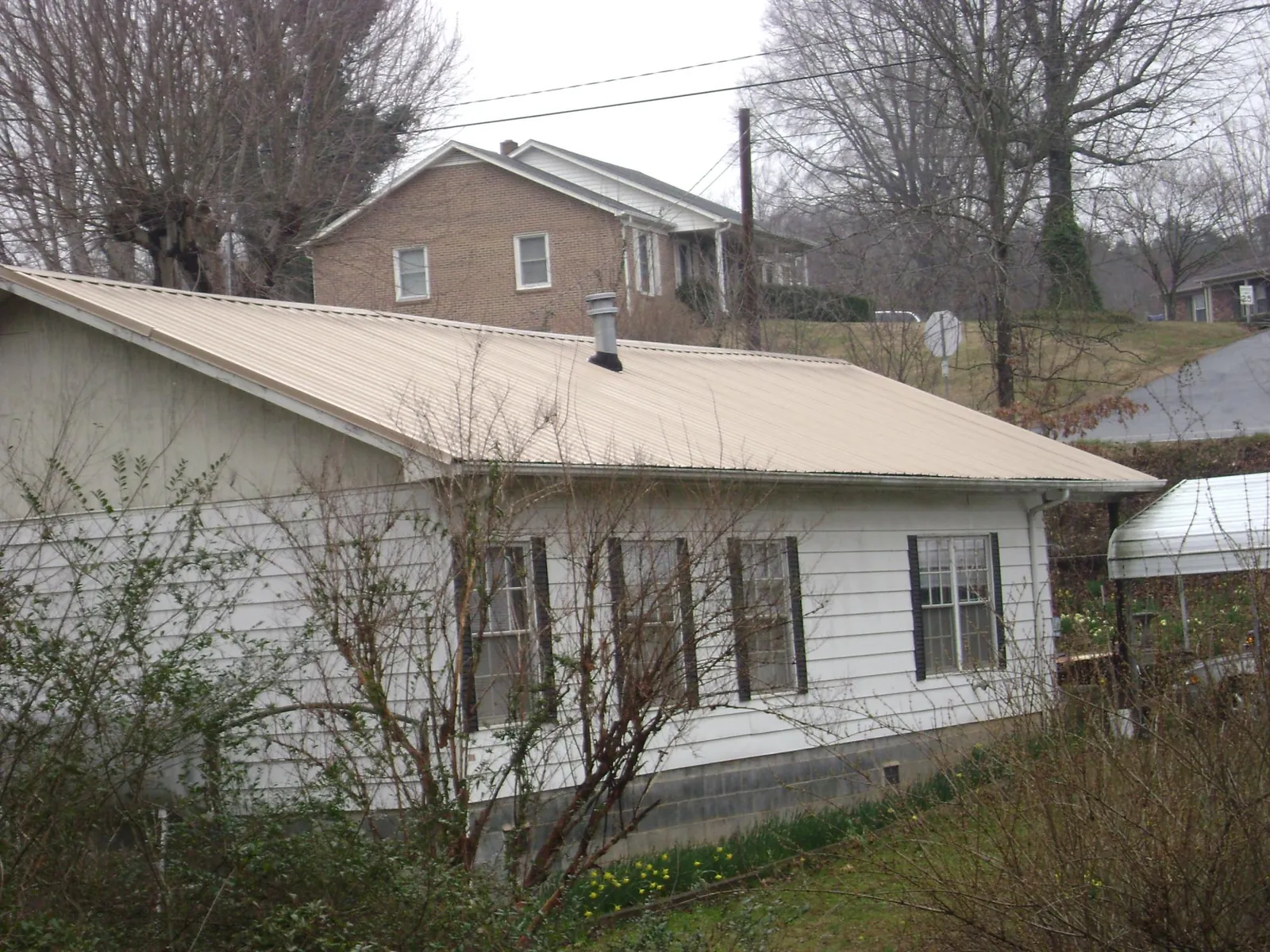 Tan metal roof on a white sided house set into a hillside — Commercial Roofing by Roofing Brothers in East Liberty